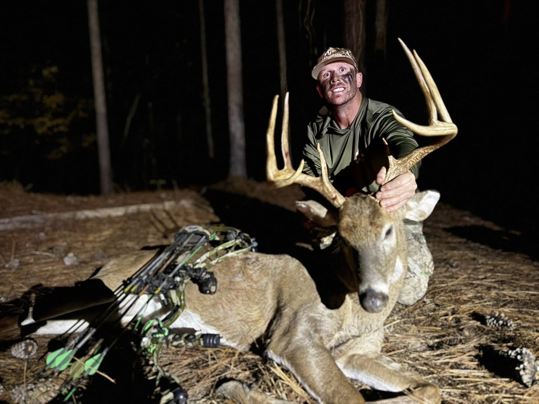 A bowhunter kneeling behind a mature whitetail buck at night