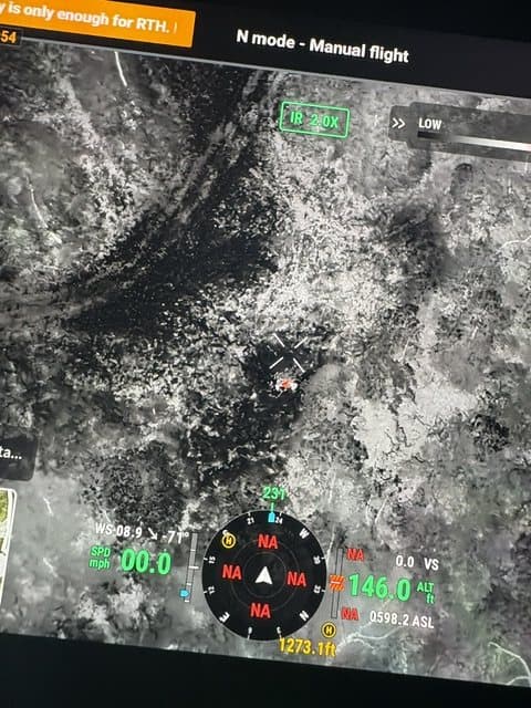 Drone controller screen showing a black-and-white thermal view over open ground